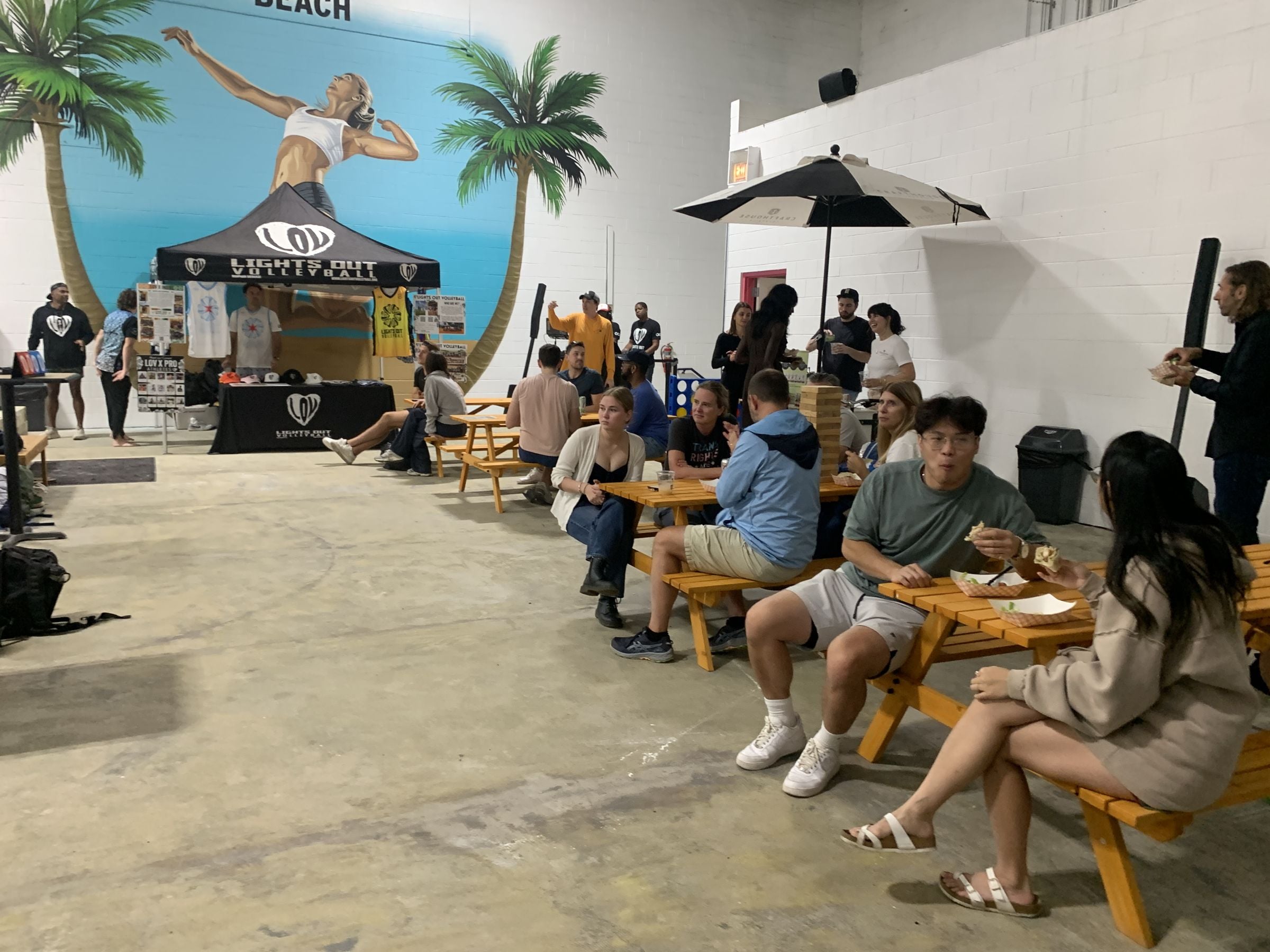 Guests eating and hanging out at picnic tables during an event at Players Sports Center, with the Players Beach mural behind